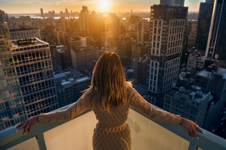 Mujer rica disfrutando del atardecer desde el balcón de un apartamentos de lujo en la ciudad de Nueva York.
