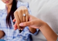 Anillo de compromiso de diamante en la mano de una mujer sostenida por su prometido.