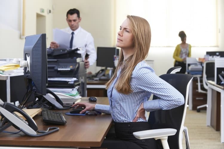 Mujer sentada en su escritorio que sufre de dolor de espalda