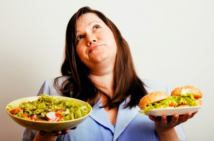 Mujer gorda eligiendo entre una hamburguesa y ensalada