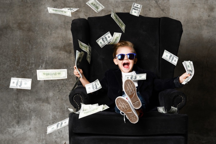 Niño rico sentado en un sillón y tirando dinero efectivo en dólares