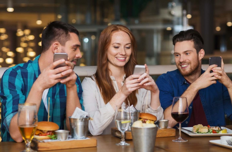 Amigos con teléfonos inteligentes cenando en un restaurante
