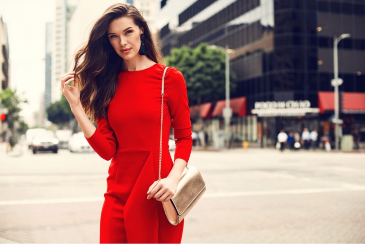 Hermosa mujer con un vestido rojo y bolso de oro, caminando por la calle.