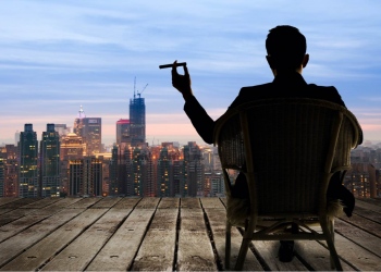 Empresario sentado en una silla sosteniendo un puro y mirando a la ciudad en la noche.