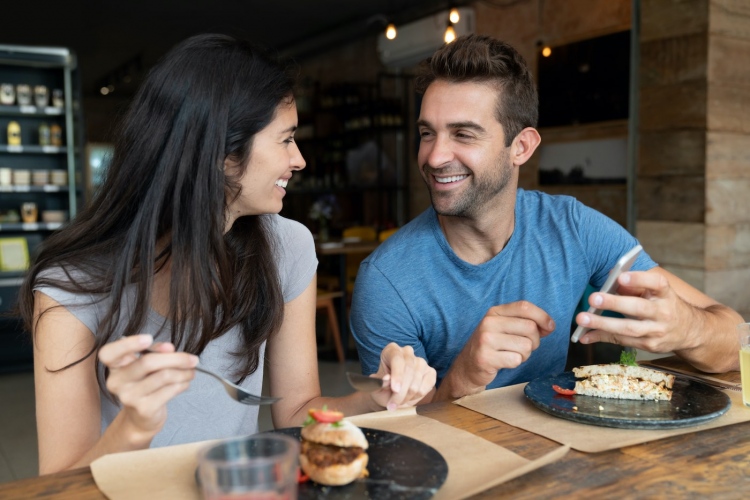 Pareja comiendo juntos en un café y mirando las redes sociales en un teléfono celular