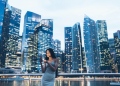 Mujer asiática mirando un teléfono inteligente con la ciudad detrás.