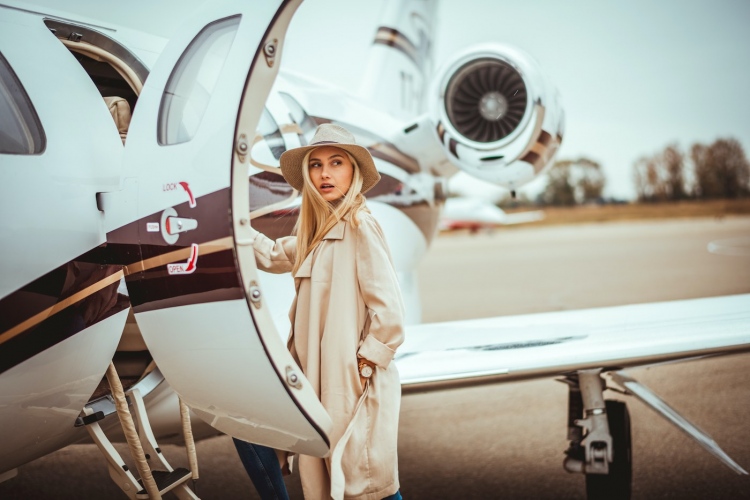 Joven mujer rubia rica entrando en un avión privado estacionado en el aeropuerto.