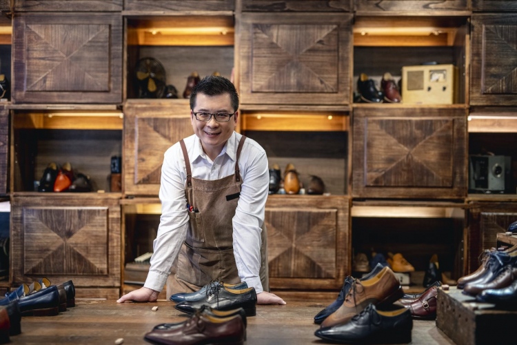 Exitoso comerciante taiwanés masculino en su tienda de zapatos de vestir para hombres.