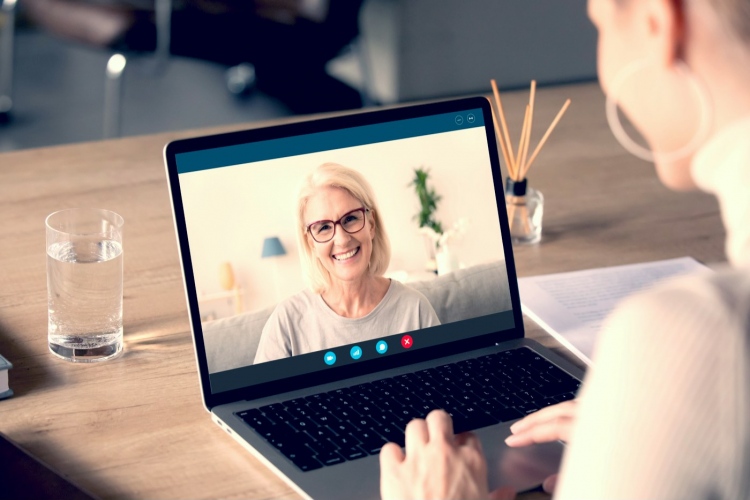 Mujer joven habla en una videollamada en la computadora con una mujer anciana sonriente.