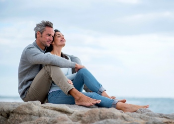 Pareja de mediana edad sentada en una roca en la playa