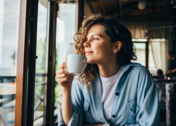 Mujer tomando café mirando por la ventana de un restaurante.