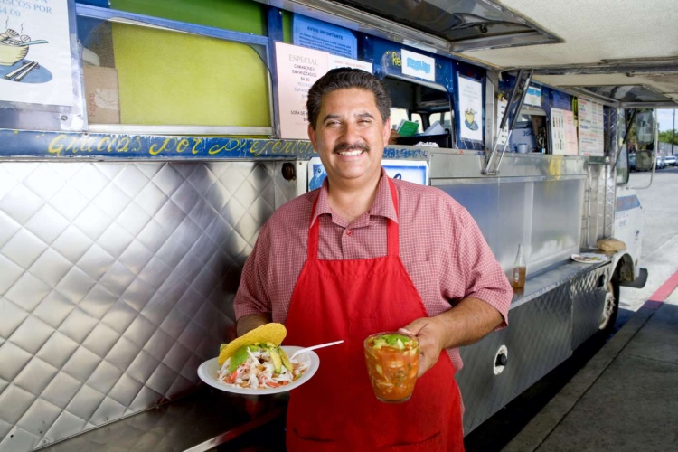 Hombre hispano con merienda y refresco junto a un camión de comida.