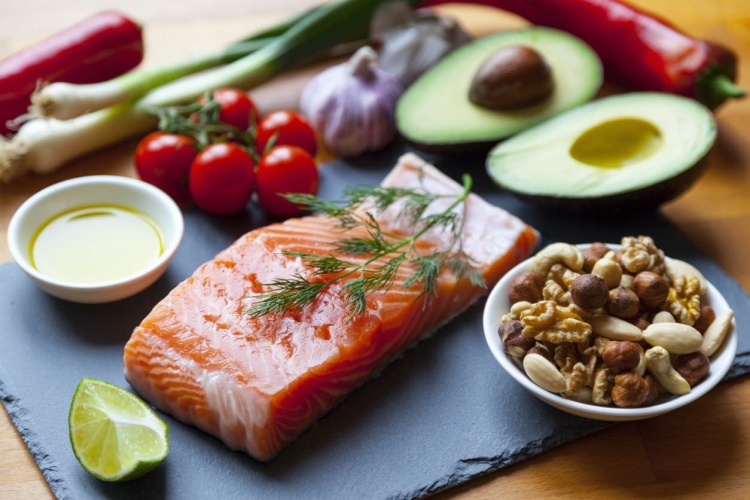 Alimentos ricos en grasas saludables como salmón, aceite de oliva, nueces y aguacates con verduras y hierbas.