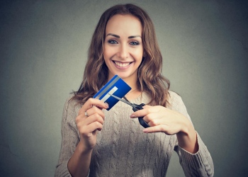 Mujer joven alegre cortando tarjetas de crédito.