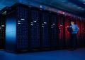 Centro de datos, especialista en TI camina por la fila de racks de servidores con una computadora portátil. Telecomunicaciones, computación en la nube, inteligencia artificial, supercomputadora.