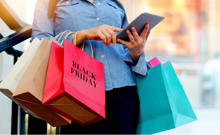 Mujer usa tableta y sostiene el bolso de compras de Black Friday.