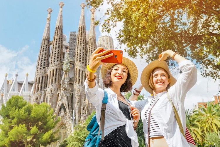 Mujeres tomando fotos selfie en su teléfono inteligente frente a la catedral católica de la Sagrada Familia en Barcelona, España.