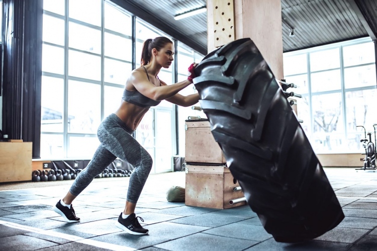 Atractiva mujer deportiva ejercitando en el gimnasio. Empujando un neumático grande.