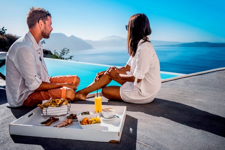 Pareja desayuna junto a una piscina infinita con vistas al océano Caldera de Santorini, Grecia.