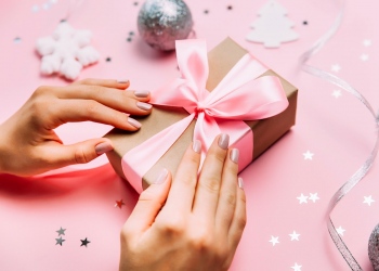 Manos femeninas con manicura de moda con caja de regalo sobre fondo festivo de Navidad.