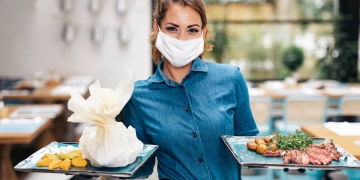 Joven camarera con máscara protectora facial trabajando en restaurante exclusivo.