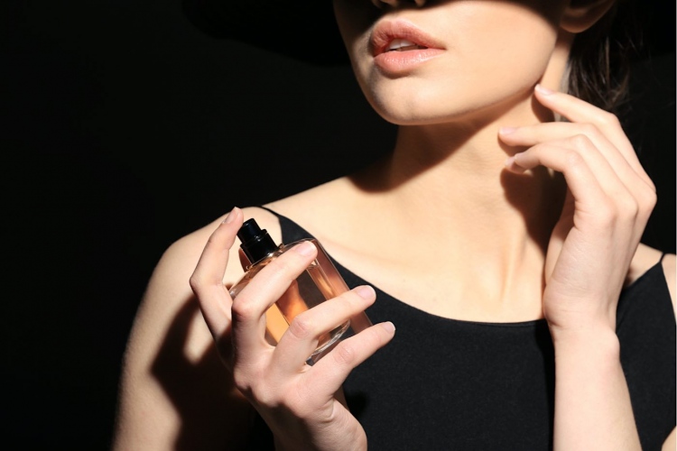 Mujer joven con botella de perfume sobre fondo oscuro
