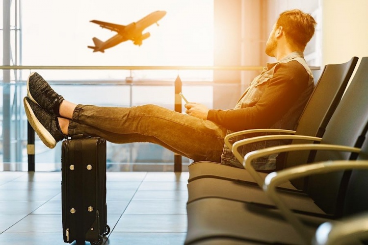 Hombre sentado en un aeropuerto viendo un avión comercial a distancia.