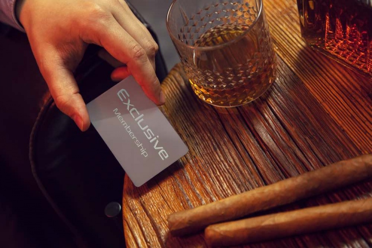 Hombre pone tarjeta VIP de membresía exclusiva sobre la mesa. Socio exclusivo, whisky en jarra y puros.