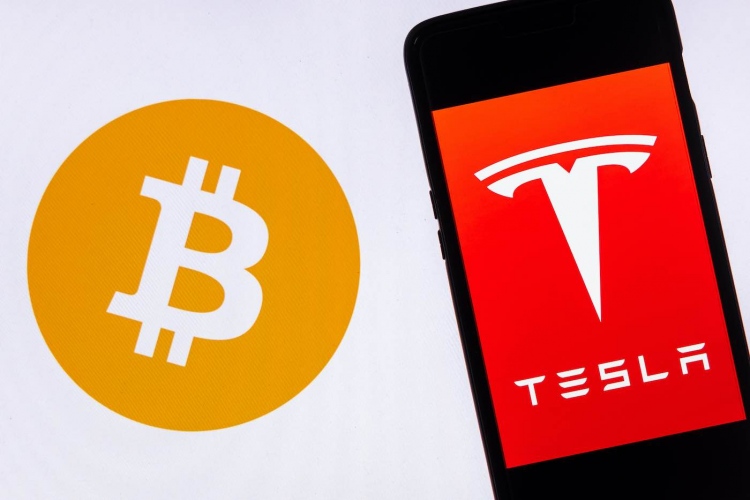 Logotipo de Tesla en un teléfono inteligente contra el logotipo de Bitcoin.