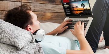Hombre mirando series de streaming en una computadora portátil, acostado en la cama.