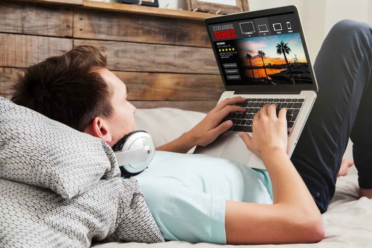Hombre mirando series de streaming en una computadora portátil, acostado en la cama.
