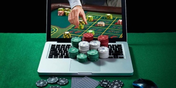 Mesa verde con fichas de casino, computadora y tarjetas en el portátil