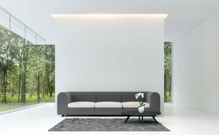 Sala de estar minimalista. Habitación blanca decorada con muebles de tela gris, decorada con alfombras grises. Grandes ventanales con vistas al jardín.
