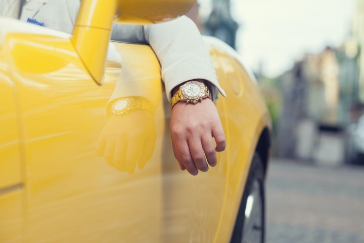 Hombre manejando coche amarillo con un reloj Rolex.