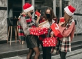Tres mujeres en ropa roja de Navidad, máscaras médicas, sombreros y regalos caminando por la ciudad y comprando en cuarentena.