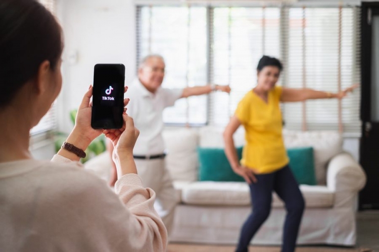 Mujer usa un teléfono móvil grabando un video de personas mayores bailando para compartir en la aplicación tiktok.