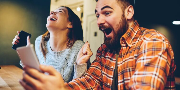 Hombres y mujeres se regocijan al ganar una lotería en Internet haciendo apuestas en un sitio web en su teléfono inteligente.