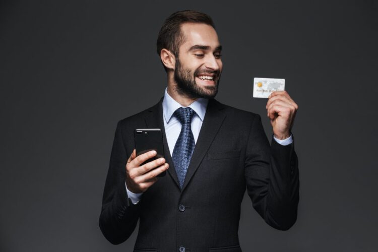 Hombre de negocios con traje usando teléfono móvil, mostrando tarjeta de crédito.