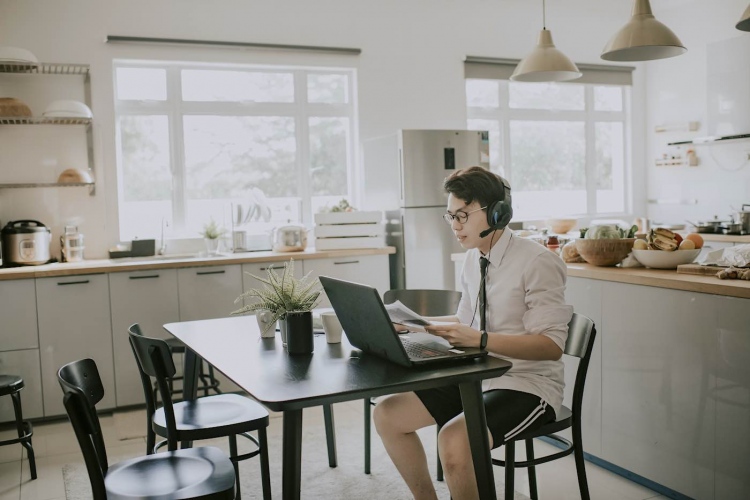 Joven asiático sentado usando una computadora portátil en su casa para una videoconferencia.